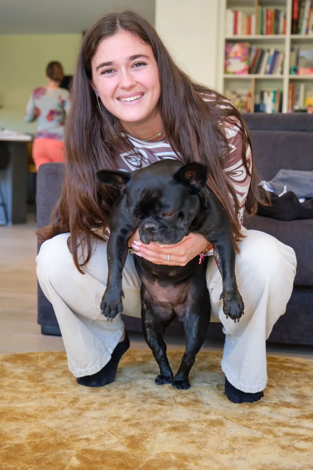 Kelly accroupie dans un salon, un bouledogue noir dans les bras